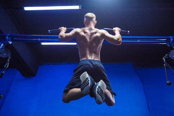Fitness man doing pull-ups in a gym for a back workout back view - Foto, Imagen