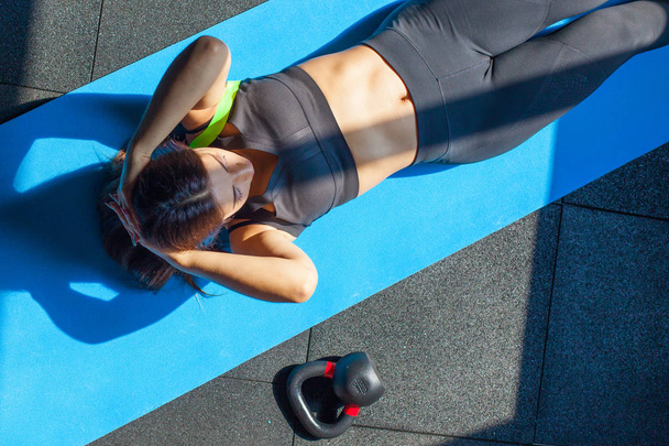 Fit young woman in sportwear lying on exercise mat near fitball and weight doing stomach exercises. Overhead view of female working out at the gym - Foto, imagen