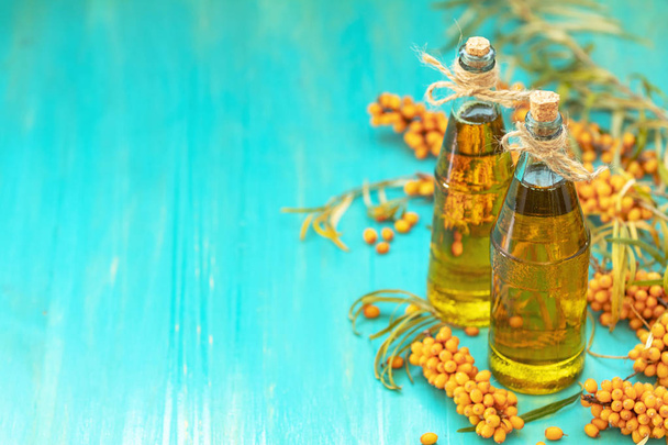 natürliches, biologisches Sanddorn- und Sanddornöl in Glasflaschen auf türkisfarbenem Holzhintergrund - Foto, Bild