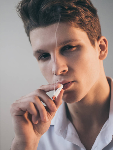Young handsome guy man smoking a cigarette, studio shooting. - Фото, зображення