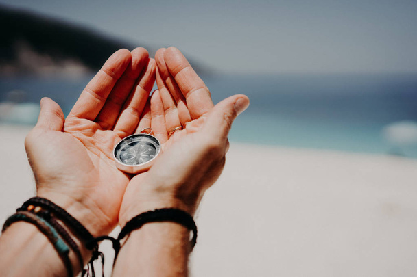 Mans hand holding compass against the backdrop of beach and sea. The concept of travel, summer vacation, holiday and journey - Foto, afbeelding