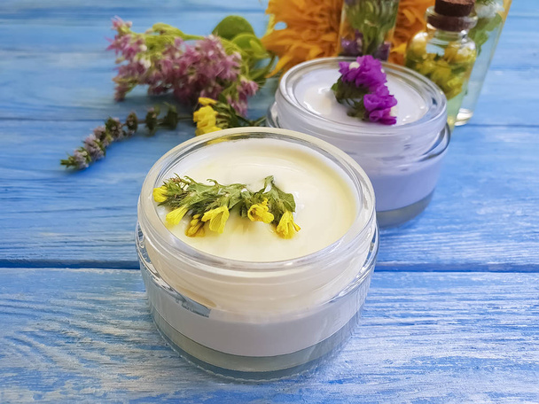 cosmetische crème, extract van bloemen op een blauwe houten achtergrond - Foto, afbeelding