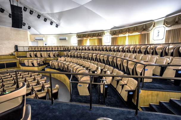 Interior brilhante de uma sala de concertos moderna com um palco e fileiras de cadeiras de couro confortáveis, um palco e sistema de amplificação acústica sob luz natural, preparado para apresentação
 - Foto, Imagem