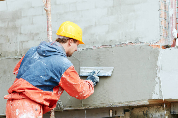 фасадные работы. строитель оштукатуривает наружную стену пластиковым ножом
 - Фото, изображение