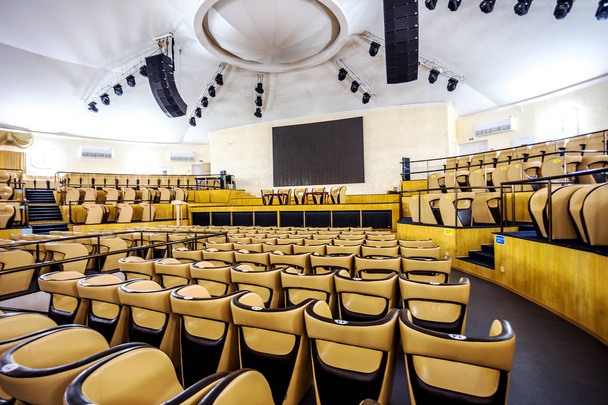 helles Interieur eines modernen Konzertsaals mit Bühne und bequemen Ledersesselreihen, Bühne und akustischem Verstärkungssystem unter Tageslicht, für die Präsentation vorbereitet - Foto, Bild