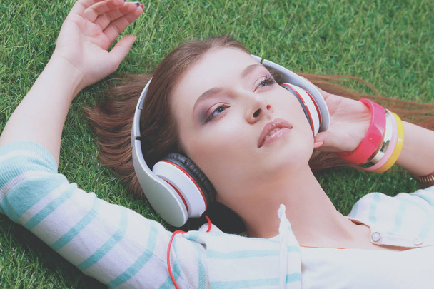 Young woman listening to the music, lying on green grass - Fotó, kép