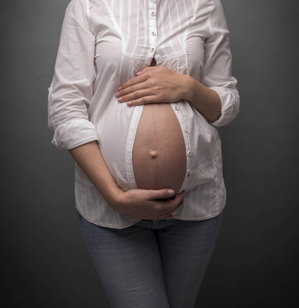 Pregnant girl with a bare belly on gray background. - Fotografie, Obrázek