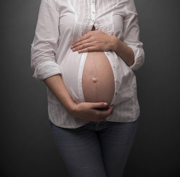 Pregnant girl with a bare belly on gray background. - Fotoğraf, Görsel