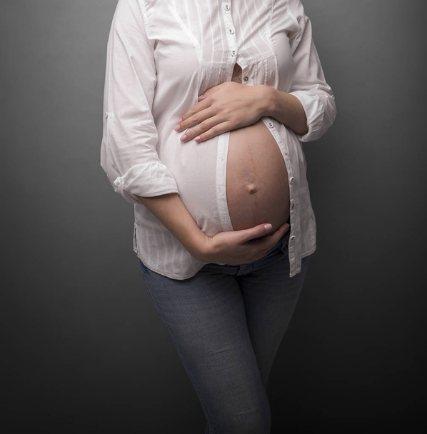 Pregnant girl with a bare belly on gray background. - Foto, afbeelding