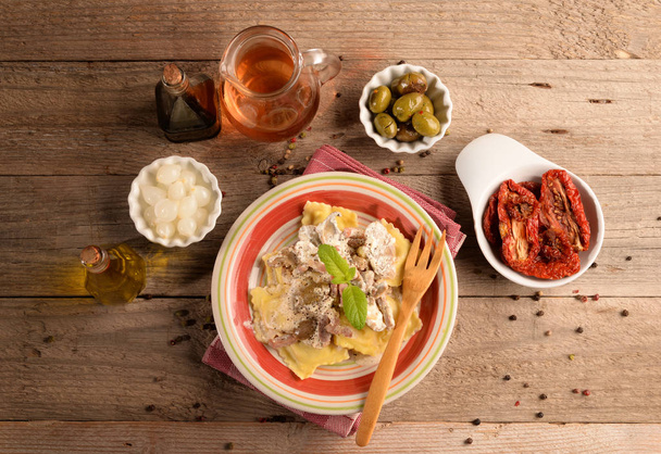 ricotta ravioli sienten ja pekonin kanssa sekä oliivien ja sipulien alkupaloja pöydällä
 - Valokuva, kuva