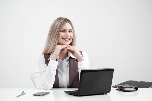 Blonde girl in a business suit works on a computer in a white bright office. - 写真・画像