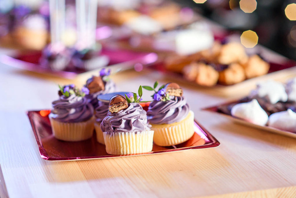 Delicious cupcakes with purple cream and candies at the holiday party. Tasty candy bar on the wooden table. - Fotografie, Obrázek