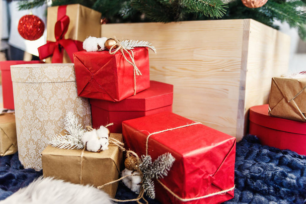 Packed in colored kraft paper holiday gift boxes under the Christmas tree. Red, gold and brown boxes near Christmas tree. - Photo, Image
