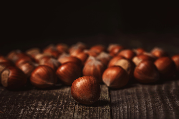 close up view of hazelnuts on wooden surface on black background - Fotó, kép