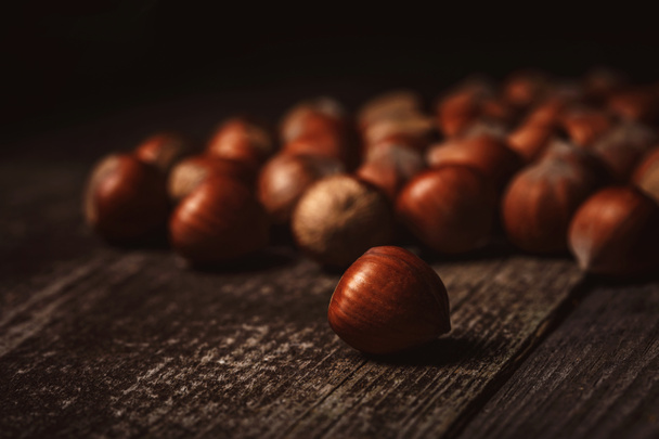 close up view of hazelnuts on wooden surface on black background - Fotografie, Obrázek