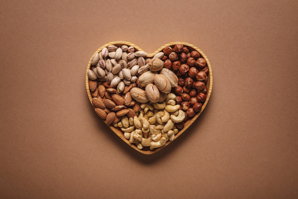 κάτοψη του ποικιλία από διάφορους ξηρούς καρπούς στην καρδιά σχήμα κουτί για καφέ σκηνικό - Φωτογραφία, εικόνα