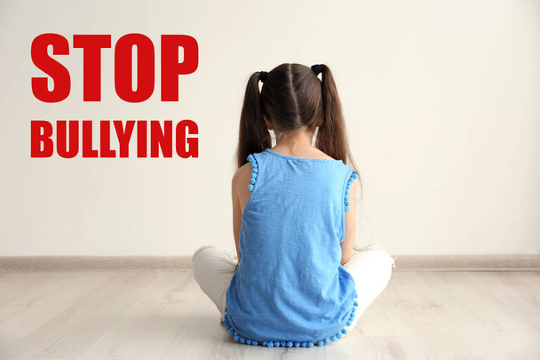 Lonely little girl sitting on floor near light wall. Message STOP BULLYING  - Foto, immagini