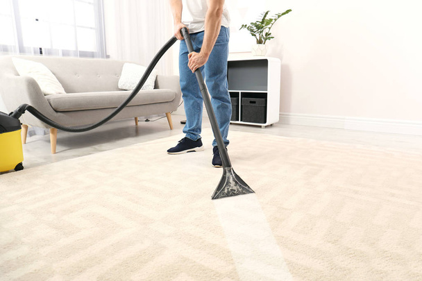 Man removing dirt from carpet with vacuum cleaner in room - Fotó, kép