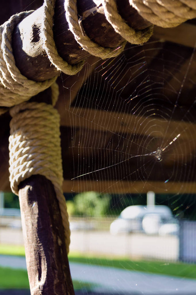 Dunne spinnenwebben in de hoek. Houten stokken vastgemaakt met een koord. De spoelen van dik touw. - Foto, afbeelding