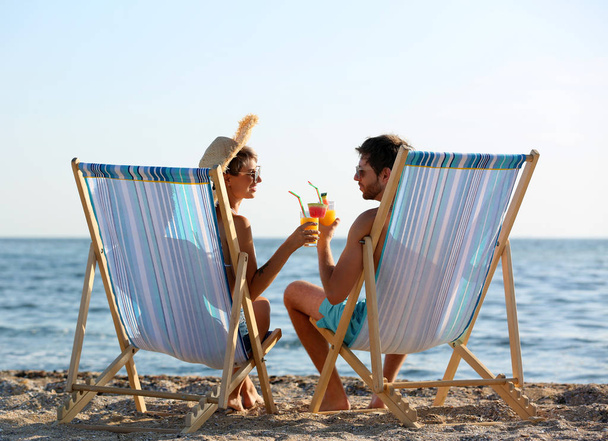 Young couple with cocktails in beach chairs at seacoast - Fotografie, Obrázek