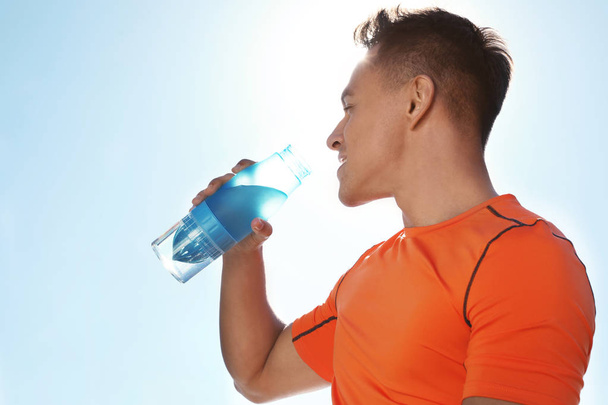 Sportowy młodego człowieka wody pitnej z butelki przeciw błękitne niebo, w słoneczny dzień. Miejsca na tekst - Zdjęcie, obraz