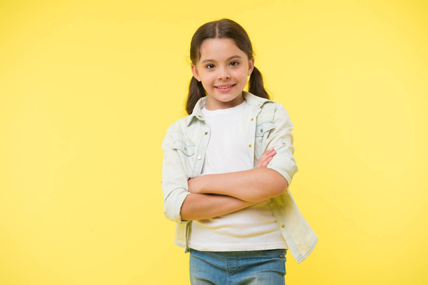 Happy confident child keep arms crossed on chest. Cheerful and confident. Little girl with cute smile. Casual look and fashion. Feel casual and confident. Small girl stand on yellow background - Фото, зображення