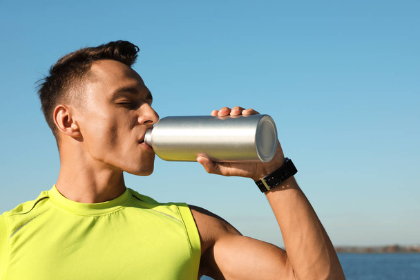 Young sporty man drinking from water bottle outdoors on sunny day - Foto, afbeelding
