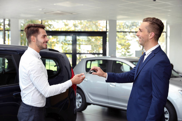 Young salesman giving car key to client in dealership - Fotografie, Obrázek