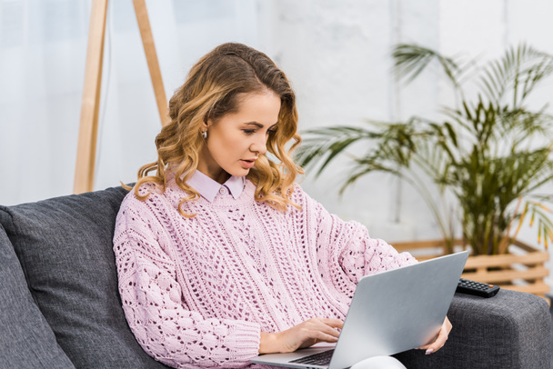 donna attraente seduta sul divano e digitando sulla tastiera del computer portatile in soggiorno
 - Foto, immagini
