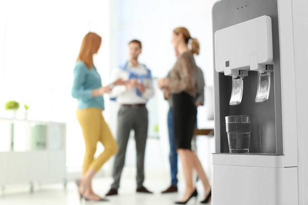 Modern water cooler with glass and blurred office employees on background. Space for text - Fotoğraf, Görsel