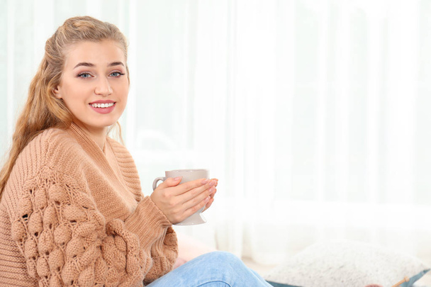 Attractive young woman in cozy warm sweater with cup of hot drink at home. Space for text - Fotografie, Obrázek