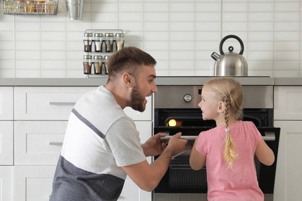 Father and daughter opening oven while baking in kitchen - Foto, Bild