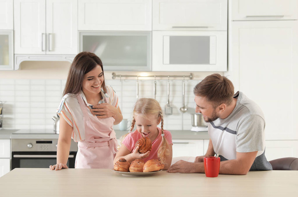 Happy couple treating their daughter with freshly oven baked bun in kitchen - Fotó, kép