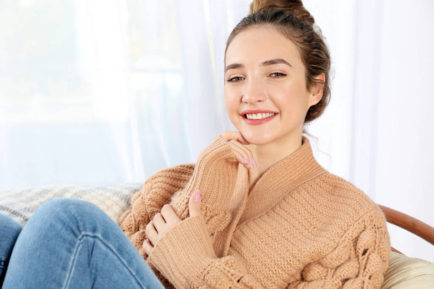 Beautiful teenage girl in warm cozy sweater sitting near window at home - Photo, image