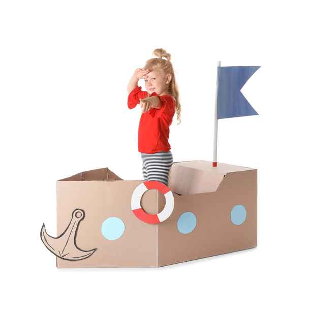Cute little girl playing with cardboard ship on white background - Foto, imagen