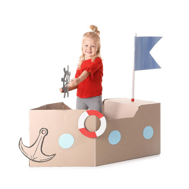 Cute little girl playing with cardboard ship on white background - Foto, Imagen