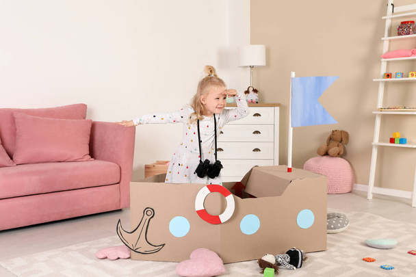 Cute little girl playing with cardboard ship at home - Fotoğraf, Görsel