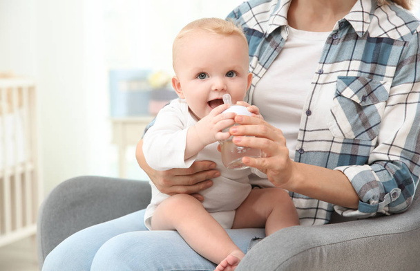 Lovely mother giving her baby drink from bottle in room - Photo, Image