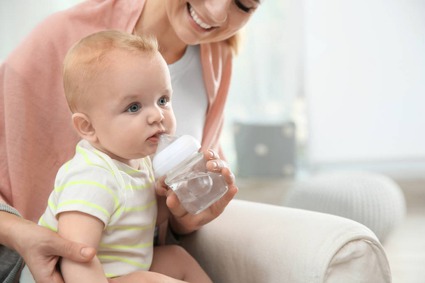 Lovely mother giving her baby drink from bottle in room - Foto, afbeelding