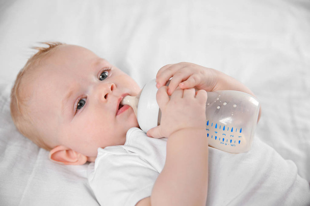 Baby drinking milk from bottle on bed, closeup - Foto, afbeelding