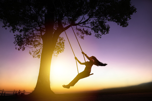 silhouette of happy young woman on a swing with sunset backgroun - Photo, Image