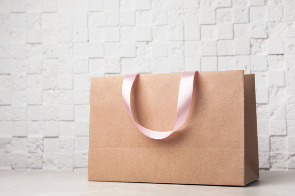 Paper shopping bag with ribbon handles on table near white wall. Mockup for design - Φωτογραφία, εικόνα