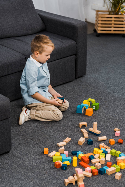 cute preschooler with multicolored wooden blocks sitting on floor in living room - Fotoğraf, Görsel