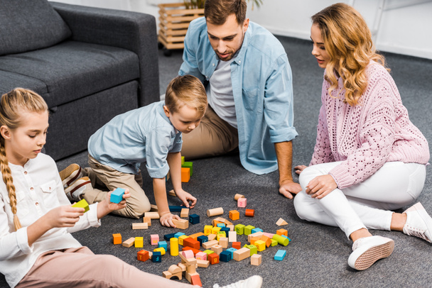 parents and siblings playing with wooden blocks on floor in living room - Foto, afbeelding