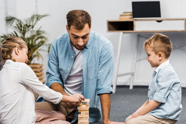 padre jugando bloques de madera juego de torre con hija e hijo en el suelo en la sala de estar
 - Foto, imagen