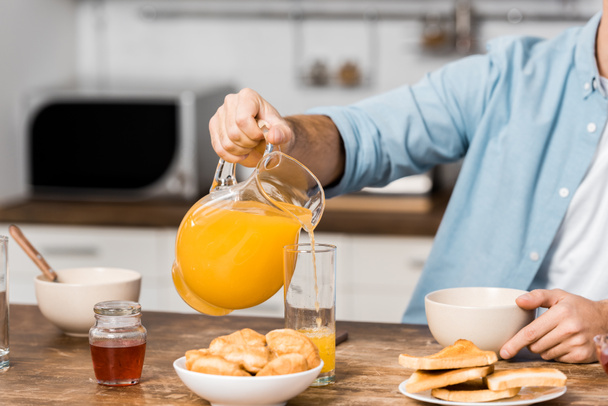 cropped view of man pouring orange juice in glass on kitchen table - Photo, Image