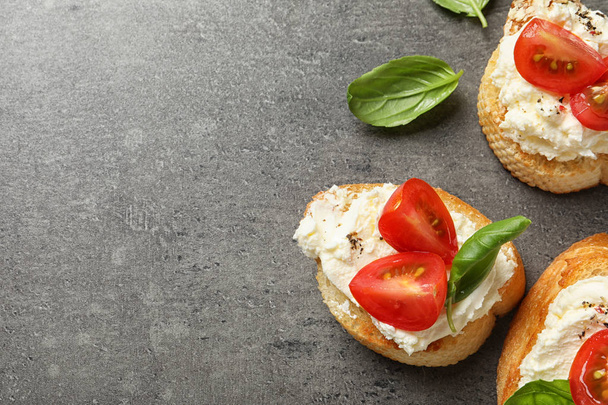 Pieces of baguette with tasty cream cheese and tomatoes on gray table, flat lay. Space for text - Foto, Imagem