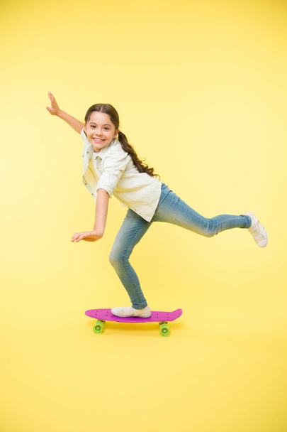 Kid having fun with penny board. Hobby favorite activity. Child smiling face stand on skateboard. Penny board cute colorful skateboard for girls. Lets ride. Girl ride penny board yellow background - Фото, изображение