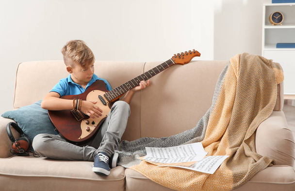 Cute little boy playing guitar on sofa in room. Space for text - Foto, Bild