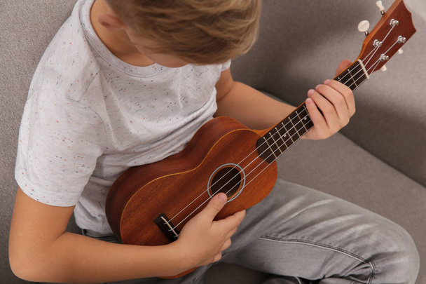 Little boy playing guitar on sofa in room, closeup - 写真・画像